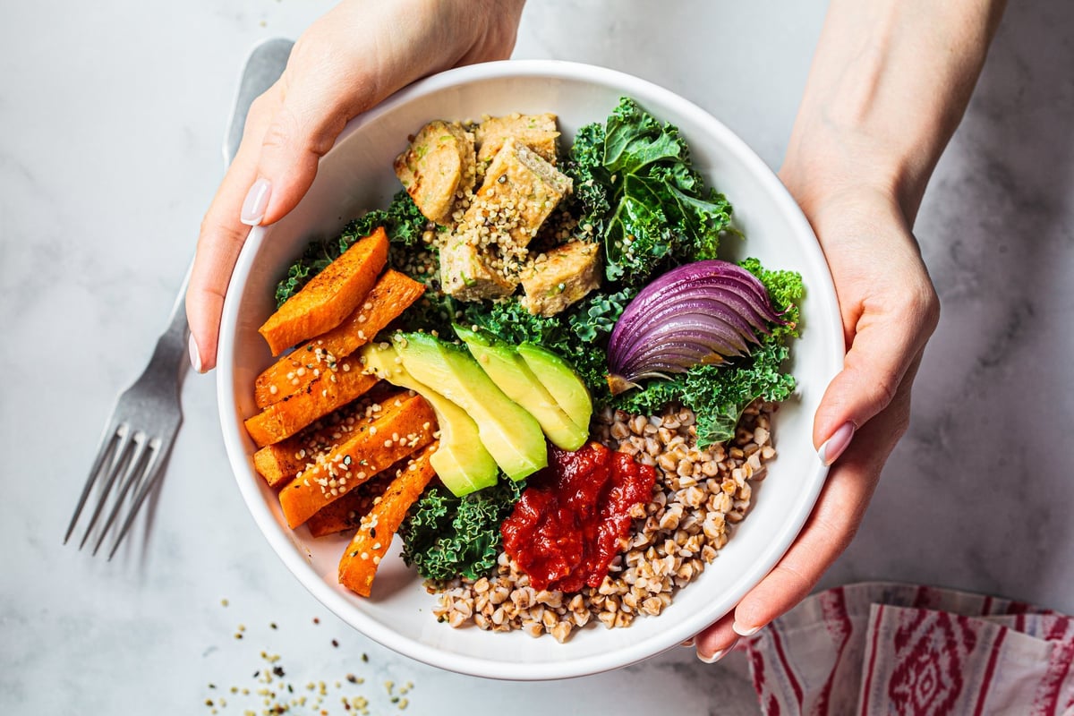 Baked vegetables, avocado, tofu and buckwheat buddha bowl. Vegan lunch salad with kale, baked sweet potato, tofu, buckwheat and avocado in a white bowl