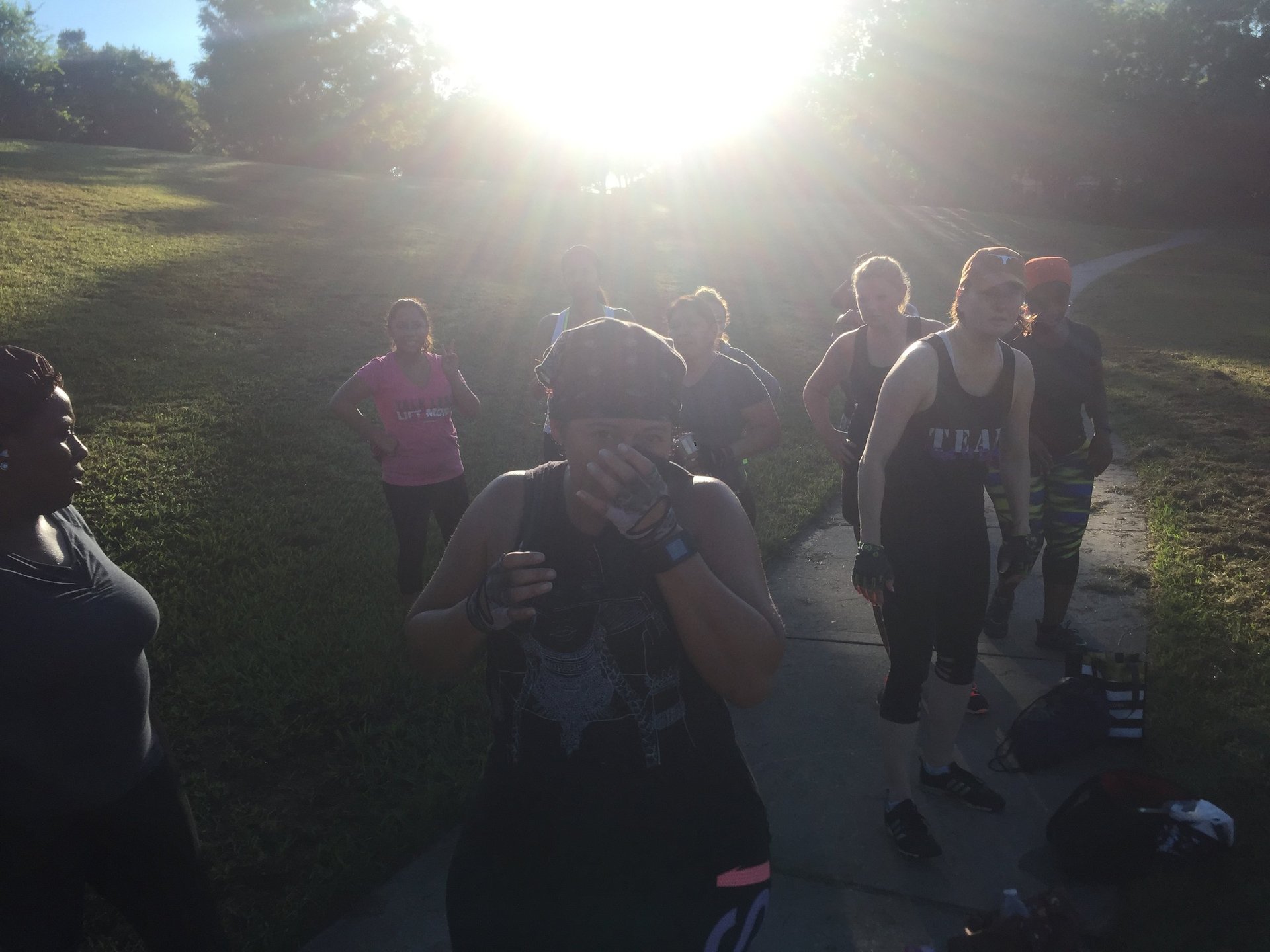 Group of runners gathered on a park path at sunset or sunrise with bright sun in background