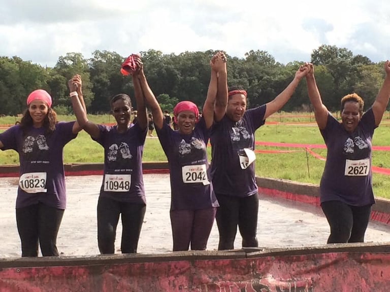 Group of runners in black shirts and pink caps raising joined hands at finish line of outdoor race event
