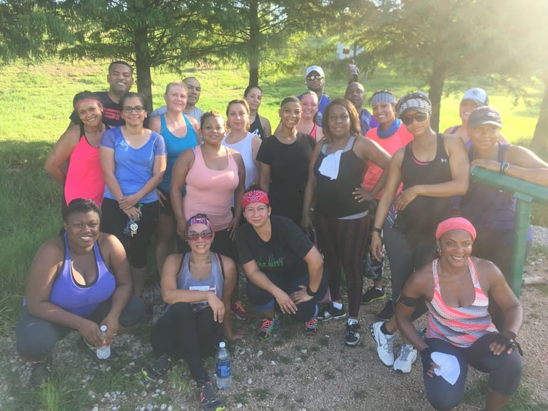 Large group of women in athletic wear posing together outdoors in a park with green grass and trees