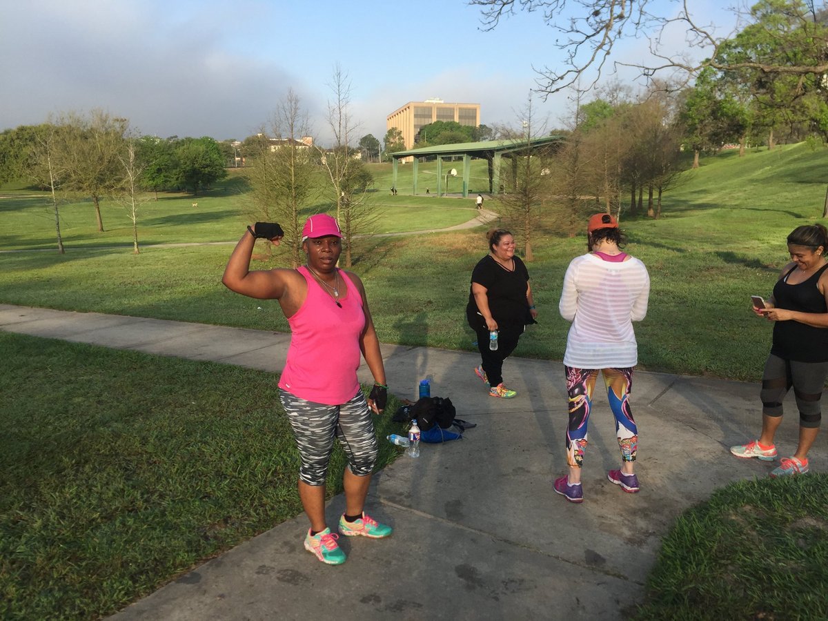 Group of five people exercising outdoors in a park, with a woman in pink leading the workout
