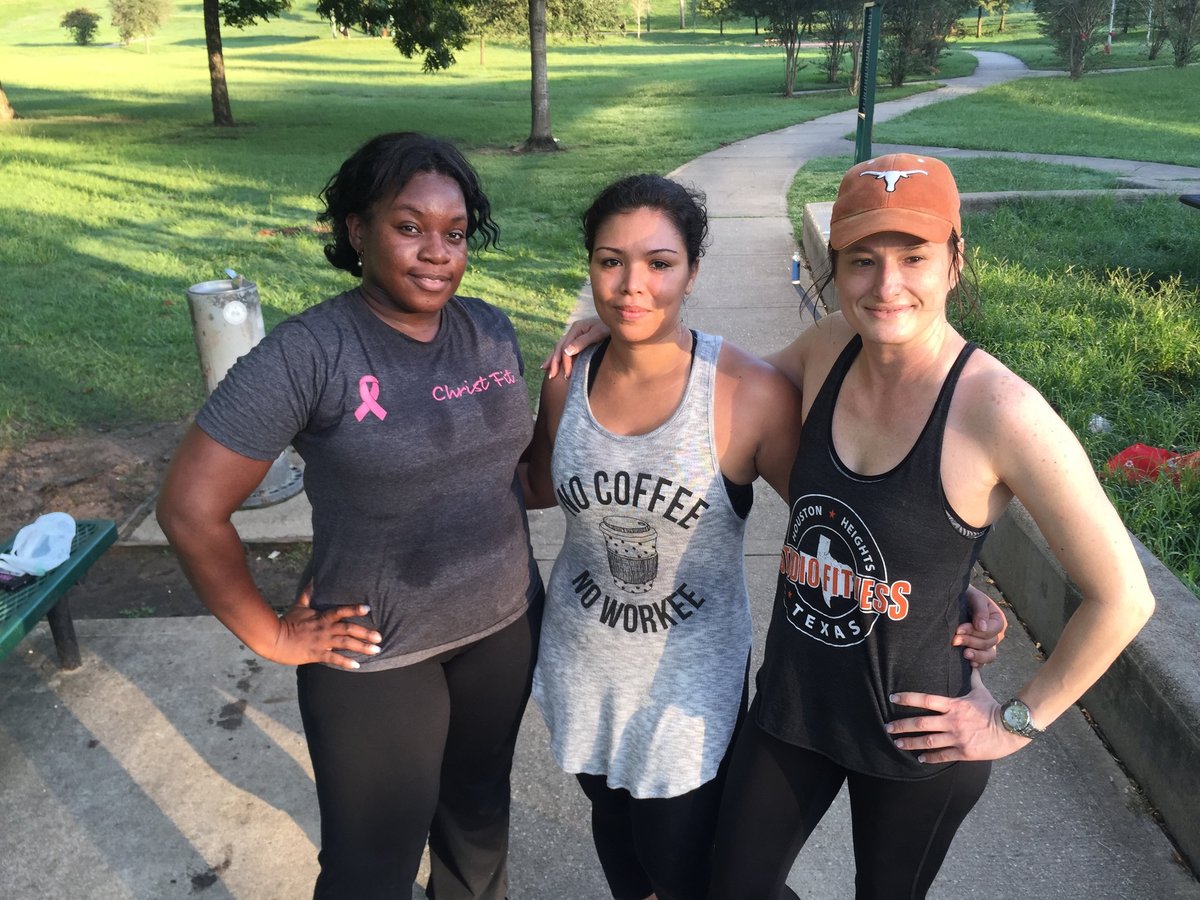 Three women posing together outdoors in a park with trees and grass in the background